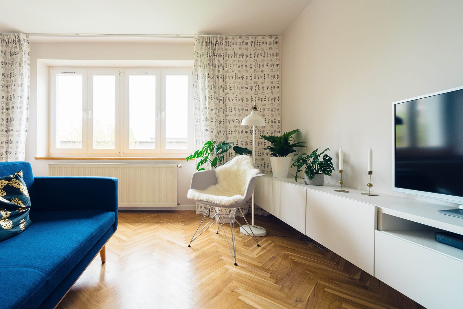 Living room with a blue sofa, a herringbone wood floor and a long white media unit