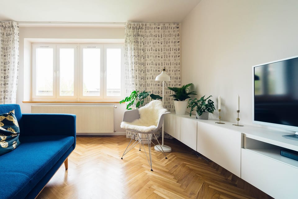 Living room with a blue sofa, a herringbone wood floor and a long white media unit