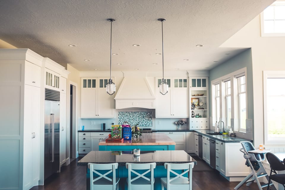 Bright kitchen with white cabinets, pendant lights and an island with teal stools