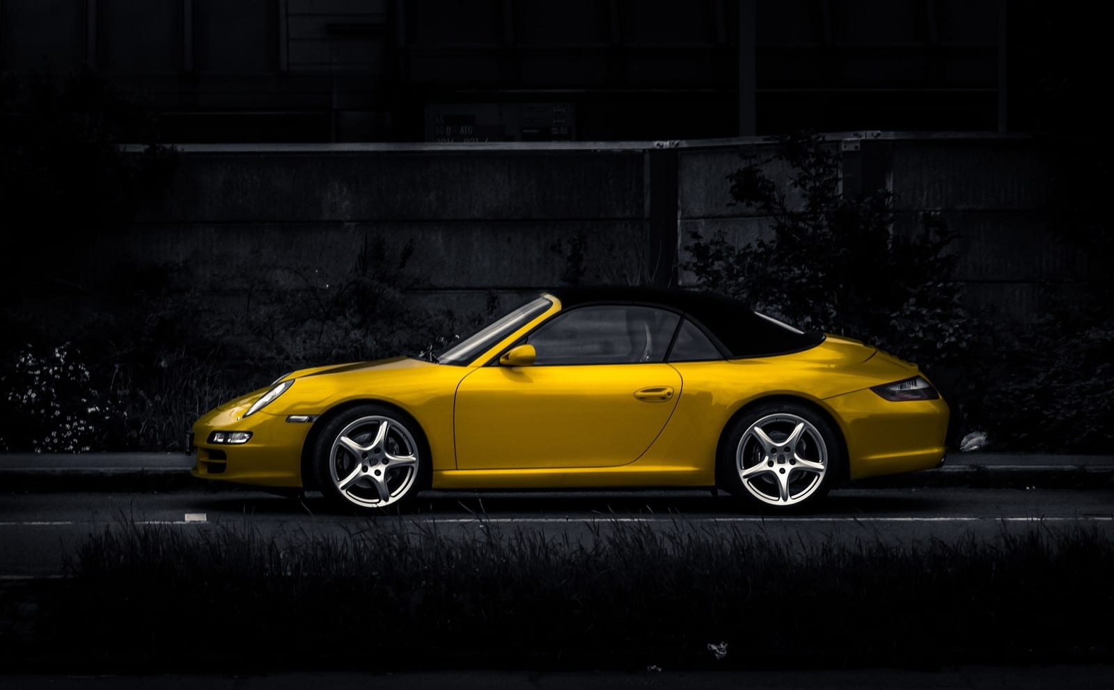 Yellow Porsche 911 convertible in profile against a dark background